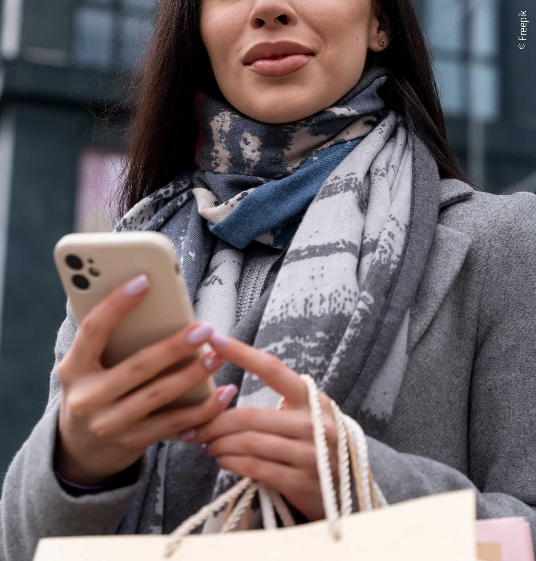 Woman shopping in the city while using her phone, illustrating consumer buying behavior.