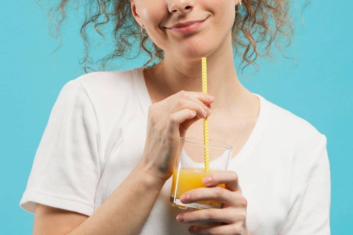 Femme souriante tenant un verre de boisson sans alcool avec une paille, illustrant la dégustation en test consommateur